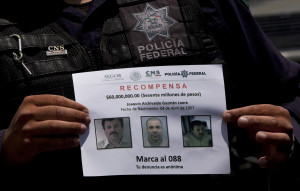 A Federal Police shows a reward notice for information leading to the capture of drug lord Joaquin "El Chapo" Guzman, who made his escape from the Altiplano maximum security prison via an underground tunnel,  in Almoloya, west of Mexico City, Thursday, July 16, 2015. The Mexican government is offering a reward of $3.8 million (60 million pesos) for Guzman's recapture. (AP Photo/Marco Ugarte)